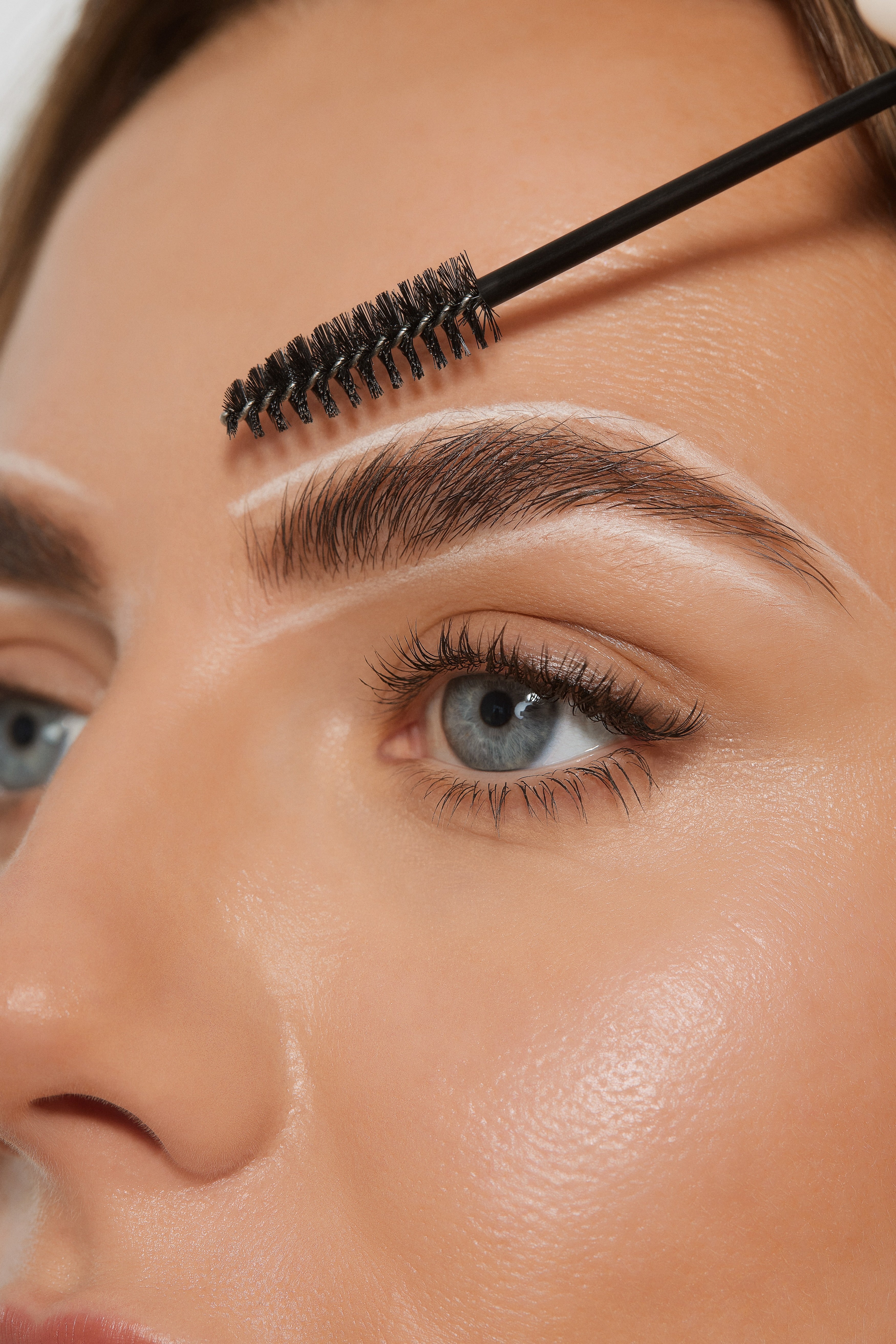 Close-up of a woman's eyebrows with white lines traced around them and a brow brush, illustrating microblading and microshading procedures for fuller brows.